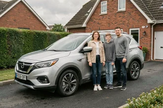 Une famille de quatre personnes souriante devant un SUV hybride argenté dans une allée de banlieue résidentielle