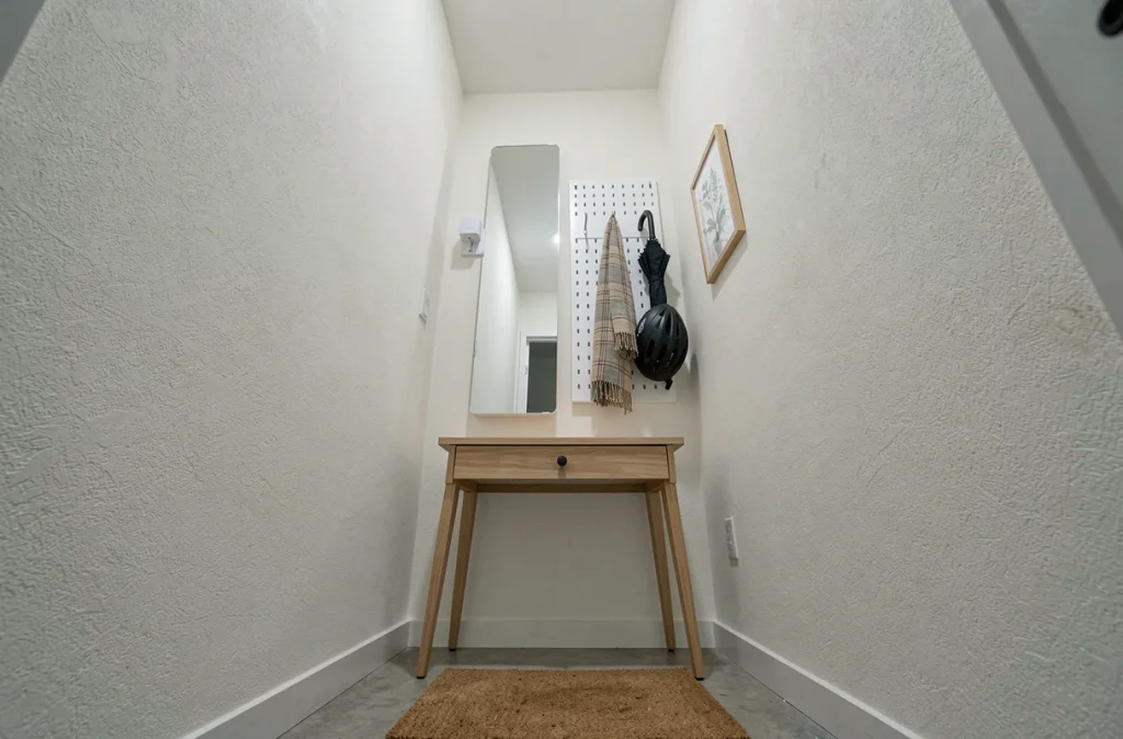 Vue en hauteur d'une entrée très étroite avec miroir, pegboard et console fine pour optimiser le rangement vertical