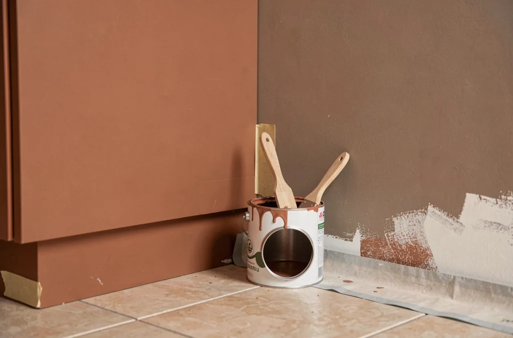 Détail d'un mur de cuisine en cours de peinture avec des teintes tendance terracotta et beige argileux et un pot de peinture ouvert